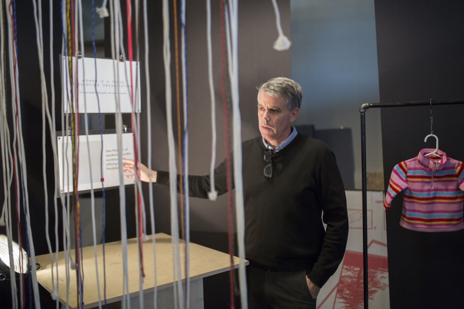 A co-founder inside the exhibit among cords hanging from the ceiling, gesturing visitors toward a suspended card