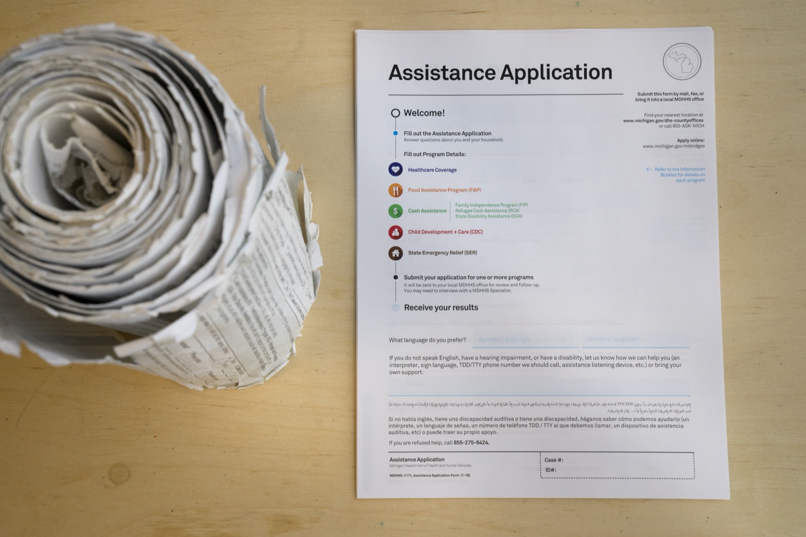 Michigan's old benefits application, rolled into a thick scroll of paper, lying next to the redesigned application's single welcome page